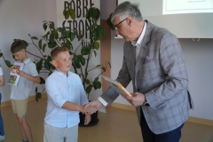 Pan Dyrektor wręcza nagrodę książkową chłopcu z klasy drugiej za zajęcie jednego z czołowych miejsc.