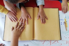 Książka zadrukowana alfabetem Braillea w dłoniach dzieci.