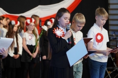 Trójka uczniów czyta opisy pieśni patriotycznych, które zostaną wykonane przez chór.