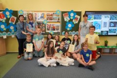 Wspólne zdjęcie organizatorów i uczestników projektu - grupa uczniów  na tle dekoracji związanej z e Świętem Niezapominajki.