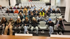 Uczniowie siedzą za stołem konferencyjnym w sali prasowej na Stadionie Narodowym. Przed nimi napis „PGE Narodowy”. Na środku serce z flagą Polski.