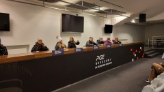 Uczniowie siedzą za stołem konferencyjnym w sali prasowej na Stadionie Narodowym. Przed nimi napis „PGE Narodowy”. Na środku serce z flagą Polski.