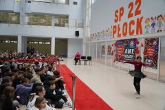 Zdjęcie przedstawia dziewczynkę tańczącą solo. Solistka ubrana jest w czarno – bordowy kostium. Dzieci siedzące na podłodze obserwują jej występ.