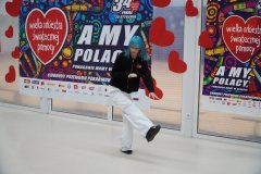 Uczennica prezentuje układ taneczny w stylu hip – hop. W tle widoczna jest dekoracja WOŚP. Tancerka ubrana jest w białe spodnie i czarną bluzę. Wyróżniają ją niebieskie włosy. 