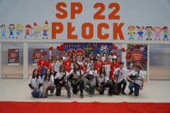 Zdjęcie przedstawia zespół muzyczny TuTu -  Band oraz chór TuTu. Zespół muzyczny prezentuje swoje  instrumenty. Dzieci ustawione są w trzech rzędach na tle napisu SP 22 Płock oraz dekoracji WOŚP. 