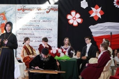 Gra Jankiel na cymbałach, obok przemawia Ksiądz Robak, w tle goście z Soplicowa i chór Tutu