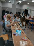 Zdjęcia przedstawiajace warsztaty plastyczne- w przestronnej sali przy ławkach ustawionych w literę "U" siedzą uczsetnicy: seniorzy i uczniowie z Koła SU, wszyscy w pogodnych nastrojach, współpracujący przy tworzeniu łapaczy promieni słońca. Na stoliczkach znajduje się mnóstwo elementów plastycznych: płyty CD, koraliki, cekiny, elementy odblaskowe itp.