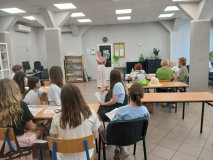 Zdjęcie wykonane w siedzibie Klubu Seniora. Przy ławkach siedzą seniorzy i przedstawiwciele SU. Wszyscy słuchają prowadzacej warsztaty fotograficzne.