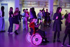 Uczniowie bawią się podczas dyskoteki andrzejkowej na przestronnej sali, oświetlonej kolorowymi światłami. 