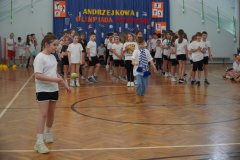 Na pierwszym planie uczennica klasy 3e i uczeń klasy 3 b biorący udział w konkurencji przenoszenia piłki tenisowej na drewnianej łyżce. W tle widoczne dzieci czekające na wykonanie zdania.
