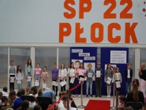 Grupa stypendystów z klas 5-6 z dyplomami w ręku, stojąca na tle ścianki dekoroacyjnej.