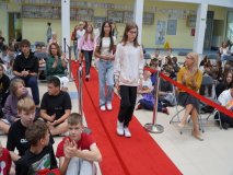Grupa stypendystów z klas 7-8 krocząca po czerwonym dywanie wsród bijącej brawo publiczności.