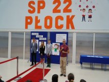 Prezentacja psychologa szkolnego, Pana Mariusza Łakomskiego, na tle występujących w apelu i ścianki dekoracyjnej.