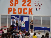 Prezentacja pedagoga szkolnego, Pani Beaty Cieśleńskiej, na tle występujących w apelu i ścianki dekoracyjnej.
