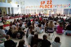 Dwoje uczniów z listami gratulacyjnymi w rękach na czerwonym dywanie w przestronnej sali, w tle klaszcząca Pani Dyrektor oraz tablice z dekoracja w tematyce sukcesu