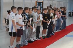 Na czerwonym dywanie w szeregu ustawiona jest grupa stypendystów z listami gratulacyjnymi. Wszyscy są w pogodnych nastrojach.