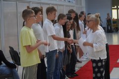 Dwie Panie Dyrektorki wręczają listy gratulacyjne grupie stypendystów stojących na czerwonym dywanie.