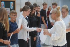Dwie Panie Dyrektorki wręczają listy gratulacyjne grupie stypendystów. Wszyscy są uśmiechnięci i radośni.