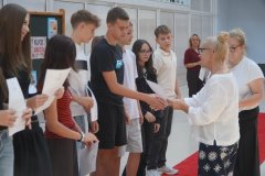 Dwie Panie Dyrektorki wręczają listy gratulacyjne grupie stypendystów stojących na czerwonym dywanie.