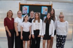 Grupa pięciu uczennic, nauczycielki i dwóch dyrektorek; w tle tablica z tematycznnymi hasłami o sukcesie.