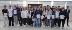 Grupa wszystkich nagrodzonych stypendystów z klas 7-8 oraz Pani Dyrektorki stojące na czerwonym dywanie podczas uroczystości wręczenia listów gratulacyjnych.
