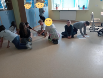 Foto_10 Na podłodze sali lekcyjnej uczestnicy zajęć w małych grupkach układają papierowe puzle