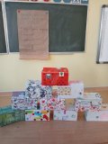 Foto_5 W sali lekcyjnej, na ławce jest ustawiony stos gotowych "pateczek pierwszej pomocy emocjonalnej"wykonanych własnoręcznioe przez uczestników zajęć z tekturowych pudełek ozdobionych kolorowymi papierami, symbolami, napisami: SKARBY, SZACUNEK, PRZYJAŹN, OPTYMIZM, SZCZEŚCIE itp., w tle zoelona tablica z plakatem przyczepionym na magnesy, a na nim ręcznie wypisane zasady (wartości) dobrej wpółpracy w grupie, które zostały ustalone z uczestnikami i prowadzącą zajęcia.