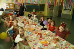 Uczniowie klasy 1F, wraz z wychowawcą, siedzą przy stole, na którym znajduje się słodki poczęstunek. Z sufitu zwisają kolorowe bibuły.