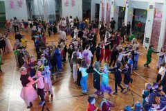 Uczniowie wszystkich klas, podczas zabawy na sali gimnastycznej, tworzą „wężyki”. W tle znajduje się dekoracja wykonana z kolorowych balonów, kurtyn oraz proporczyków.