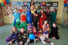 Zdjęcie grupowe Uczniów klasy 2f. Przy stole siedzą Dzieci przebrane m.in. za ufoludki, dinozaury, koty i tancerza.