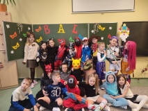  Zdjęcie grupowe Uczniów klasy 1c. Na tle karnawałowej dekoracji stoją Dzieci przebrane m.in. za superbohaterów, postacie z bajek, sportowców i zwierzątka.
