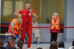 Forum szkoły. Ratownik WOPR prezentuje różnice między kamizelką asekuracyjną, a kamizelką ratunkową.
