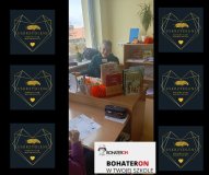 Wolontariusz prowadzący zajęcia siedzi przy biurku przy komputerze.        Na biurku widać książki, papierowe dekoracje oraz kartę pracy jednego z uczniów.