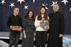 Na tle dekoracji stoją: Wicedyrektor Szkoły- p. A. Gawlińska, ksiądz P. Szulc oraz laureaci konkursu na najładniejszą szopkę bożonarodzeniową.