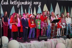 Zdjęcie przedstawia trzy solistki śpiewające kolędę oraz towarzyszący im chór TuTu.