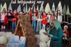 Widzimy Panią Dyrektor Marlenę Błachowicz, która składa świąteczne życzenia. Za Panią Dyrektor stoi chór.