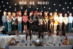 Szkolny chór Tu - tu śpiewa kolędę, uczennice występujące w przedstawieniu siedzą przy stole wigilijnym.