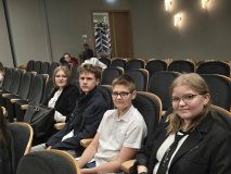 wnętrze Mediateki, na czarnych fotelach na widowni siedzi czworo Uczniów z naszej szkoły – dwie dziewczynki i dwoje chłopców, patrzą w obiektyw z uśmiechem,