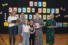 Na tle dekoracji ,,Cała Polska Czyta Dzieciom’’ stoi  Pani  Dyrektor, Nauczyciele i Uczniowie nagrodzeni za wzorowe czytelnictwo.