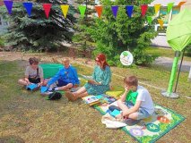 Podczas festynu rodzinnego w strefie ,,Czytanie na polanie’’ na kocu siedzi nauczyciel i czyta uczniom fragmenty literatury dziecięcej.