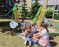 Czytanie książki dla dzieci na dworze przez Panią Iwonę z biblioteki - grupa dzieci siedząca  na trawie i słuchająca utworów. 