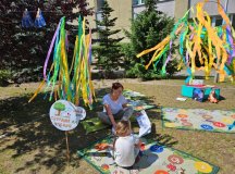 Czytanie książki dla dzieci na dworze przez Panią Iwonę z biblioteki - grupa dzieci siedząca  na trawie i słuchająca utworów. 