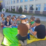 Uczniowie z klasy szóstej na trawniku przed szkołą czytają książki młodszym kolegom.