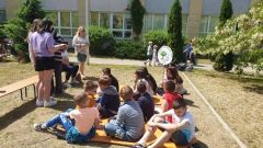 Uczniowie siedzą na trawie i słuchają czytających książkę starszych koleżanek.