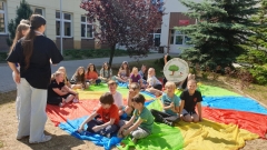 Uczniowie siedzą na trawie i słuchają czytających książkę starszych koleżanek.