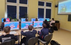 Klasa, w której uczniowie korzystają z komputerów do nauki o technologii i kreatywności, oglądają prezentację o bezpiecznym Internecie na projektorze.