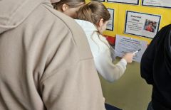 Nastolatki w szkole uczestniczące w zabawie nt. Bezpiecznego Internetu szukają informacji na gazetce szkolnej.