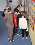Grupa zainteresowanych nastoletnich uczniów obserwujących szkolną ścianę wystawową w klasie, poszukujących nauki i wiedzy, skupiając się na czytaniu.