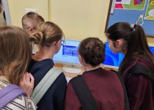 Grupa nastoletnich uczniów patrzących na ekran komputera w klasie, skupiających się na nauczaniu cyfrowym i technologii w edukacji.