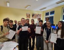 Grupa szczęśliwych uczniów trzymających certyfikaty uznania w klasie, świętujących swoje osiągnięcia w szkole.